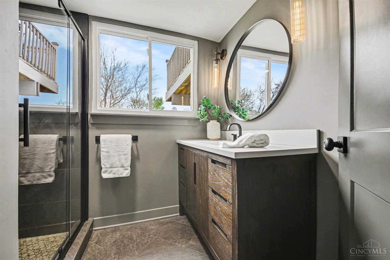 7230 Barret Road West Chester, OH 45069 - Photo 27 of 50 The downstairs bath exudes dark, modern, and moody — showcasing an oversized wood vanity with quartz top, high-end fluted dark brass light fixtures, wood floating shelves, black herringbone floors that coordinate perfectly with the luxury tiled shower with glass pivot door.