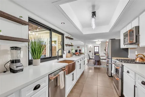 a large white kitchen with stainless steel appliances a lot of counter space and a window