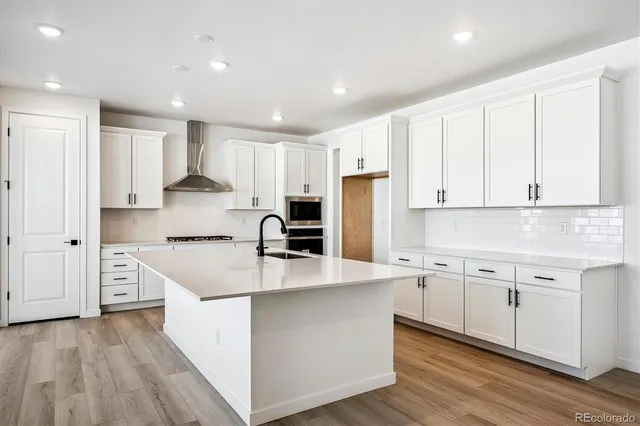 a large kitchen with stainless steel appliances granite countertop a stove a sink a refrigerator and white cabinets with wooden floor