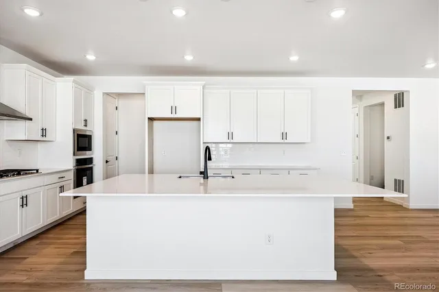 a kitchen with stainless steel appliances granite countertop a white refrigerator a stove a sink and white cabinets with wooden floor