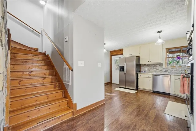 a kitchen with granite countertop a refrigerator oven a sink dishwasher and white cabinets with wooden floor