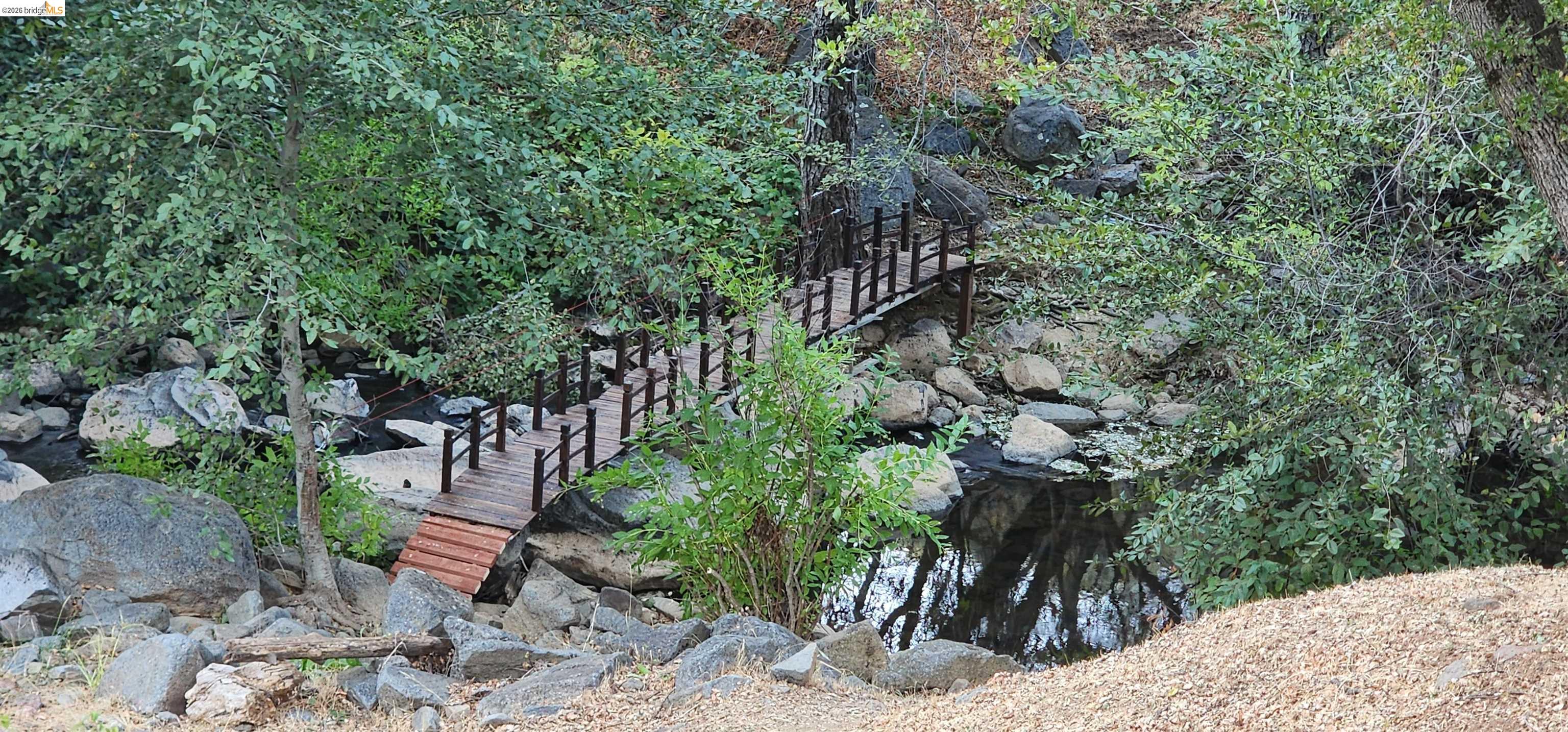 18399 Lime Kiln Road Sonora, CA 95370 - Photo 2 of 36 Wooden footbridge crossing a natural creek, surrounded by established trees and natural rock formations