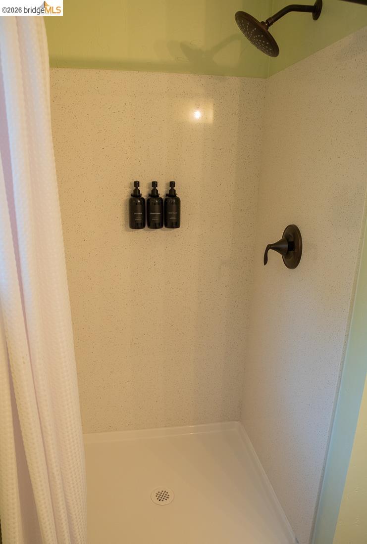 18399 Lime Kiln Road Sonora, CA 95370 - Photo 28 of 36 Shower stall featuring a white base, textured wall panels, a bronze-finish rainfall showerhead, and a matching bronze-finish single-handle faucet