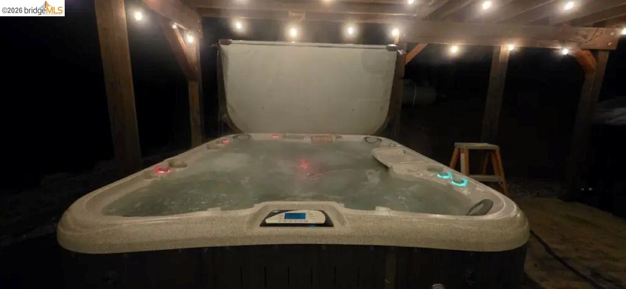18399 Lime Kiln Road Sonora, CA 95370 - Photo 31 of 36 Outdoor spa area featuring a large hot tub with integrated lighting, set under a wooden pergola with string lights, and surrounded by exposed wood beams