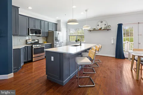 a living room with stainless steel appliances granite countertop furniture wooden floor and a kitchen view