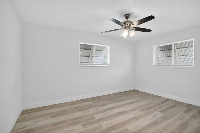 a view of an empty room with wooden floor and a ceiling fan