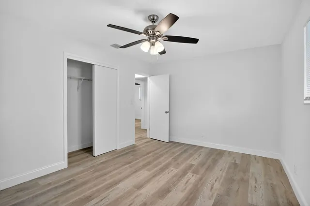 an empty room with wooden floor ceiling fan and windows