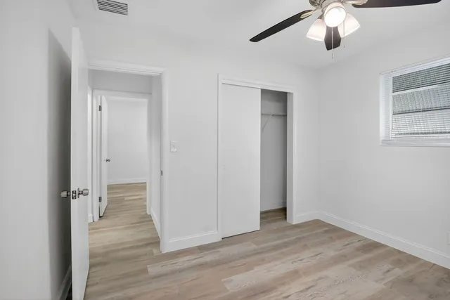 an empty room with wooden floor closet and windows