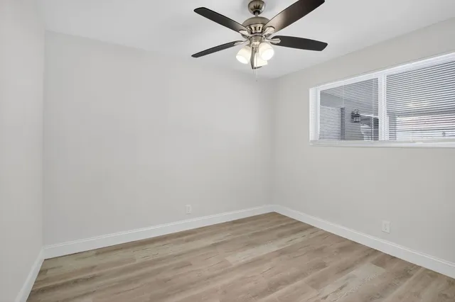 an empty room with wooden floor fan and windows