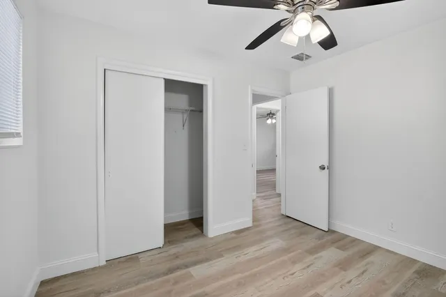 an empty room with wooden floor closet and windows