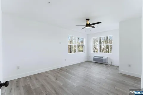 an empty room with wooden floor ceiling fan and windows