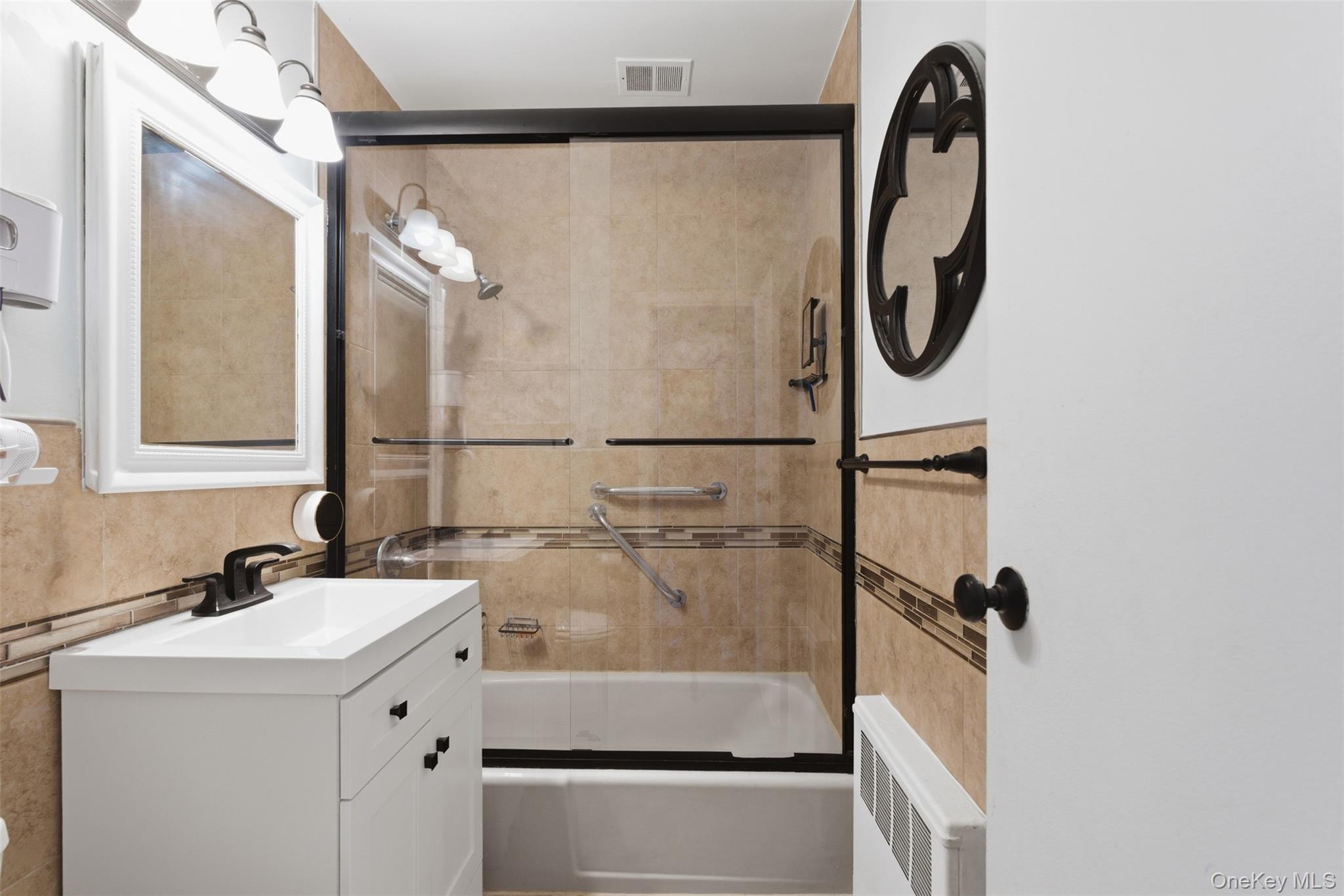 25 Trinity Place, Unit 2K New Rochelle, NY 10805 - Photo 12 of 25 Bathroom featuring a white vanity with a rectangular sink, a white-framed mirror, and a tiled shower-bathtub combination with a sliding glass door