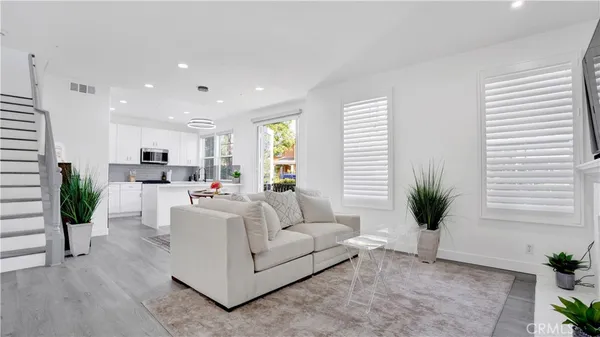 a living room with furniture a potted plant and open kitchen view