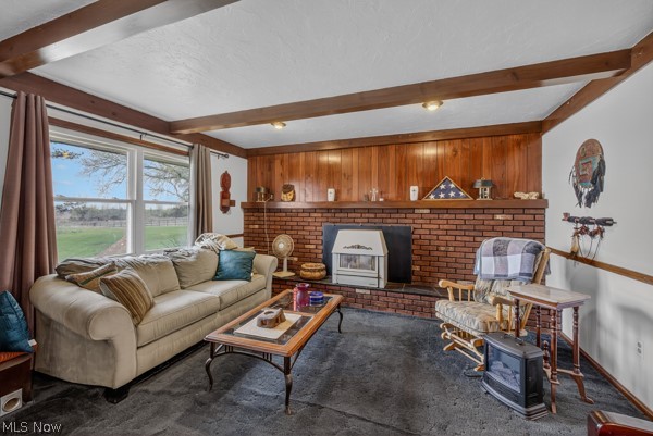 8675 West Smith Road Medina, OH 44256 - Photo 10 of 25 Living area featuring a brick fireplace with a wood-burning stove insert, wood paneling, exposed wood ceiling beams, and a large window overlooking green fields