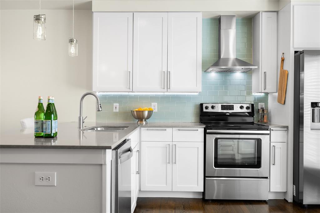 3922 Gilbert Avenue, Unit 214 Dallas, TX 75219 - Photo 2 of 27 Modern kitchen featuring white shaker cabinetry, stainless steel appliances, a light blue subway tile backsplash, a stainless steel range hood, and pendant lighting