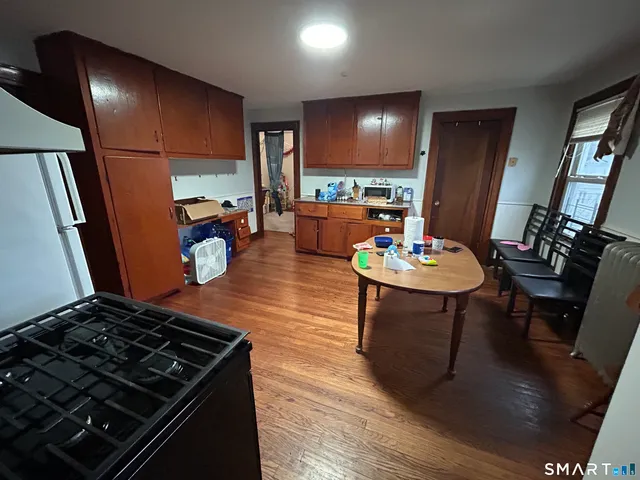 a kitchen with stainless steel appliances granite countertop a stove a refrigerator a sink a dining table and chairs with wooden floor