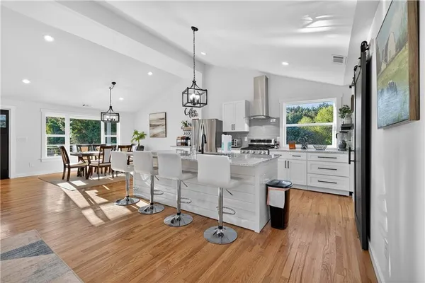 a kitchen with stainless steel appliances kitchen island granite countertop a refrigerator oven a sink dishwasher and white cabinets with wooden floor