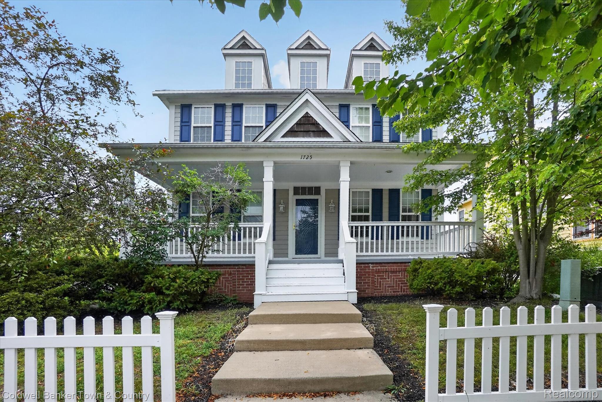 1725 Town Commons Drive Howell, MI 48855 - Photo 3 of 53 Inviting two-story residence featuring a full-width covered porch, three prominent dormers, blue window shutters, and a classic white picket fence
