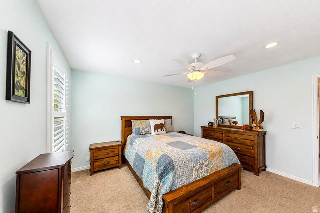 9990 Albury Road Sandy, UT 84092 - Photo 30 of 36 Spacious bedroom featuring warm wood-finish furnishings, neutral carpeting, and soft ambient lighting from a ceiling fan with integrated fixture