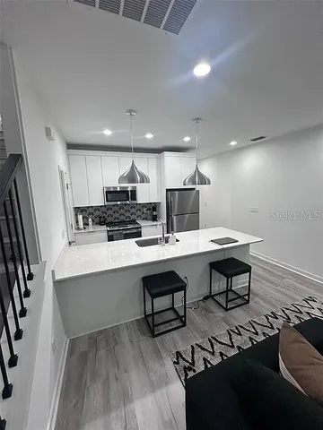 a kitchen with stainless steel appliances a dining table chairs refrigerator sink and cabinets