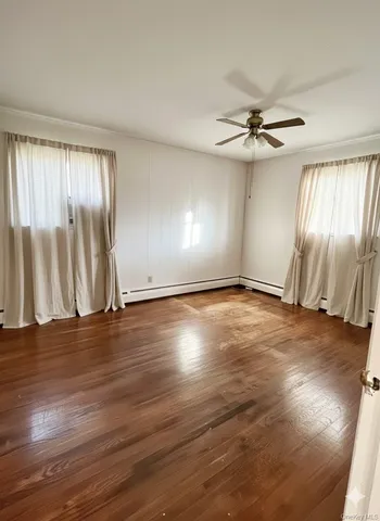 an empty room with wooden floor fan and windows