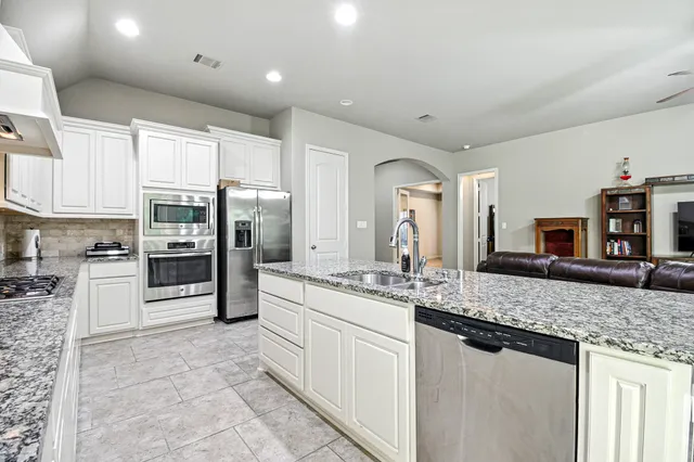 a large kitchen with stainless steel appliances a large counter top a stove a sink and a refrigerator