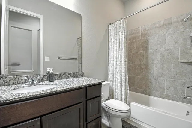a bathroom with a granite countertop sink a toilet a mirror a bathtub and shower