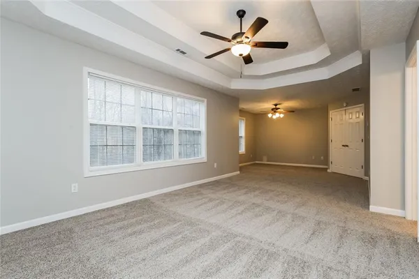 an empty room with chandelier fan and windows