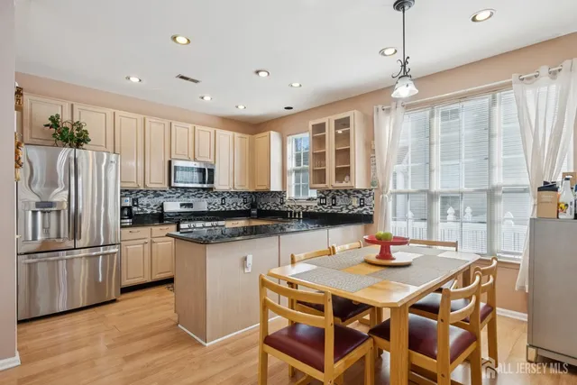 a kitchen with stainless steel appliances granite countertop a sink a stove a refrigerator cabinets and a dining table