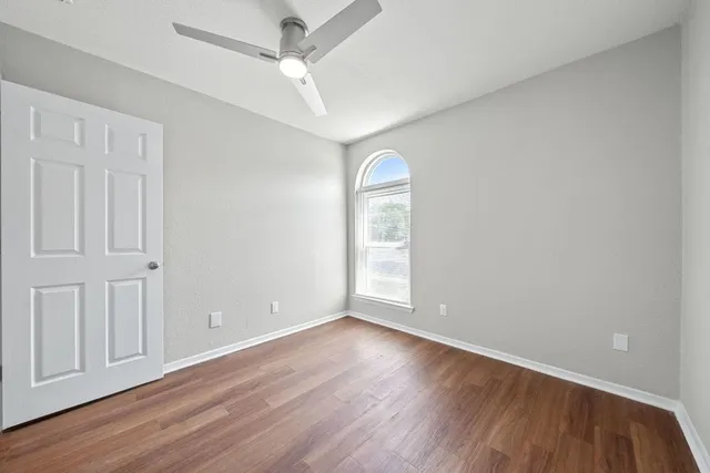an empty room with wooden floor fan and windows