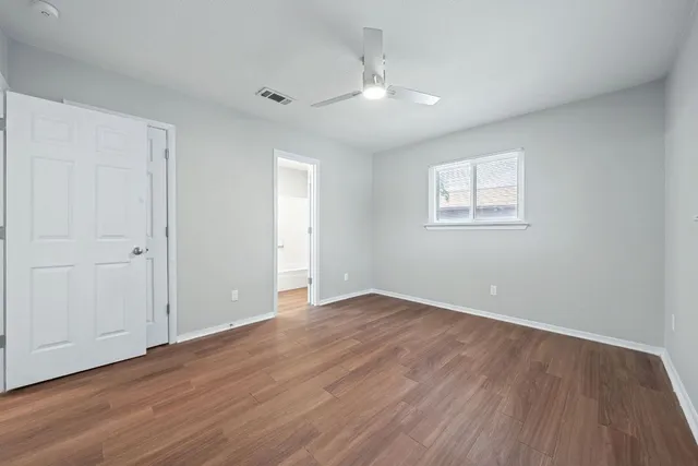an empty room with wooden floor fan and windows