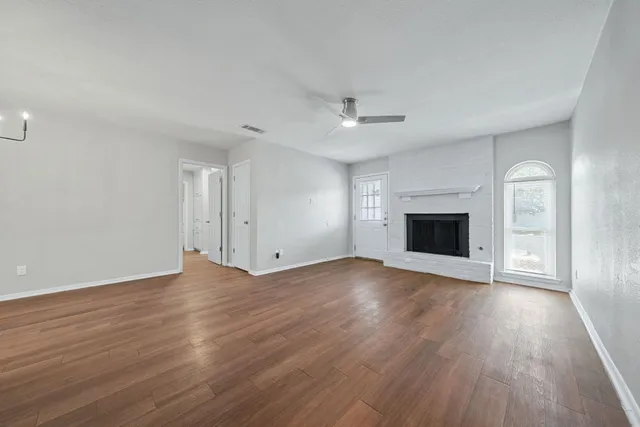 an empty room with wooden floor fireplace and windows