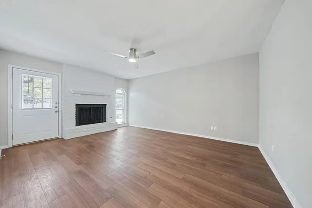 an empty room with wooden floor fireplace and windows