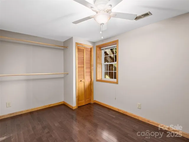 an empty room with wooden floor chandelier fan and windows