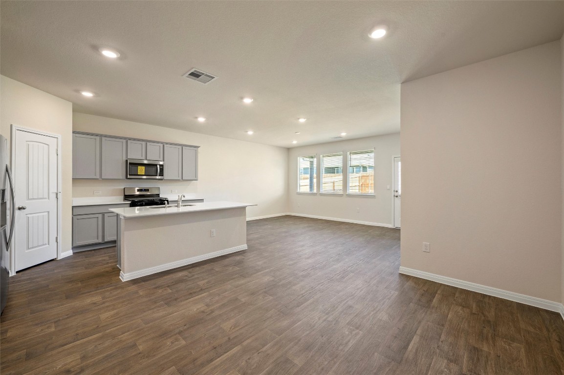 224 Kickapoo Lane Kyle, TX 78640 - Photo 29 of 31 Kitchen with gray cabinets, open floor plan, stainless steel appliances, a kitchen island with sink, and dark wood-style floors