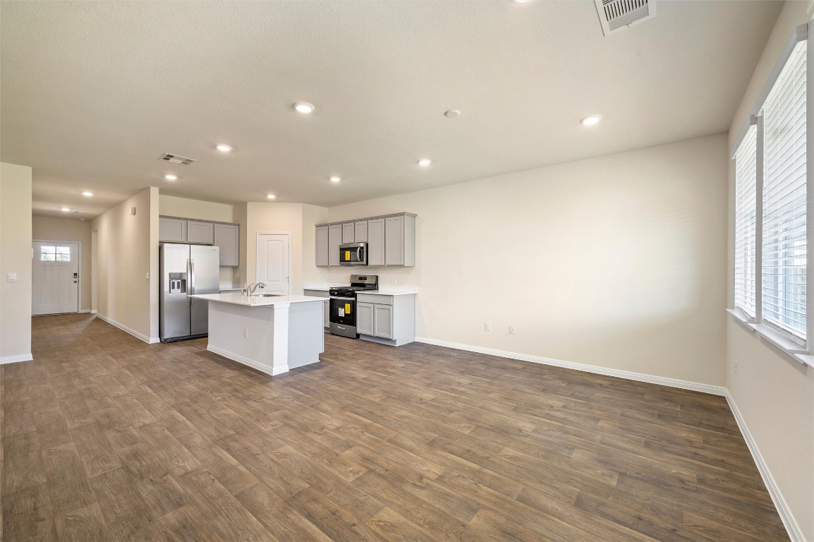 224 Kickapoo Lane Kyle, TX 78640 - Photo 31 of 31 Kitchen featuring appliances with stainless steel finishes, gray cabinetry, open floor plan, an island with sink, and light countertops