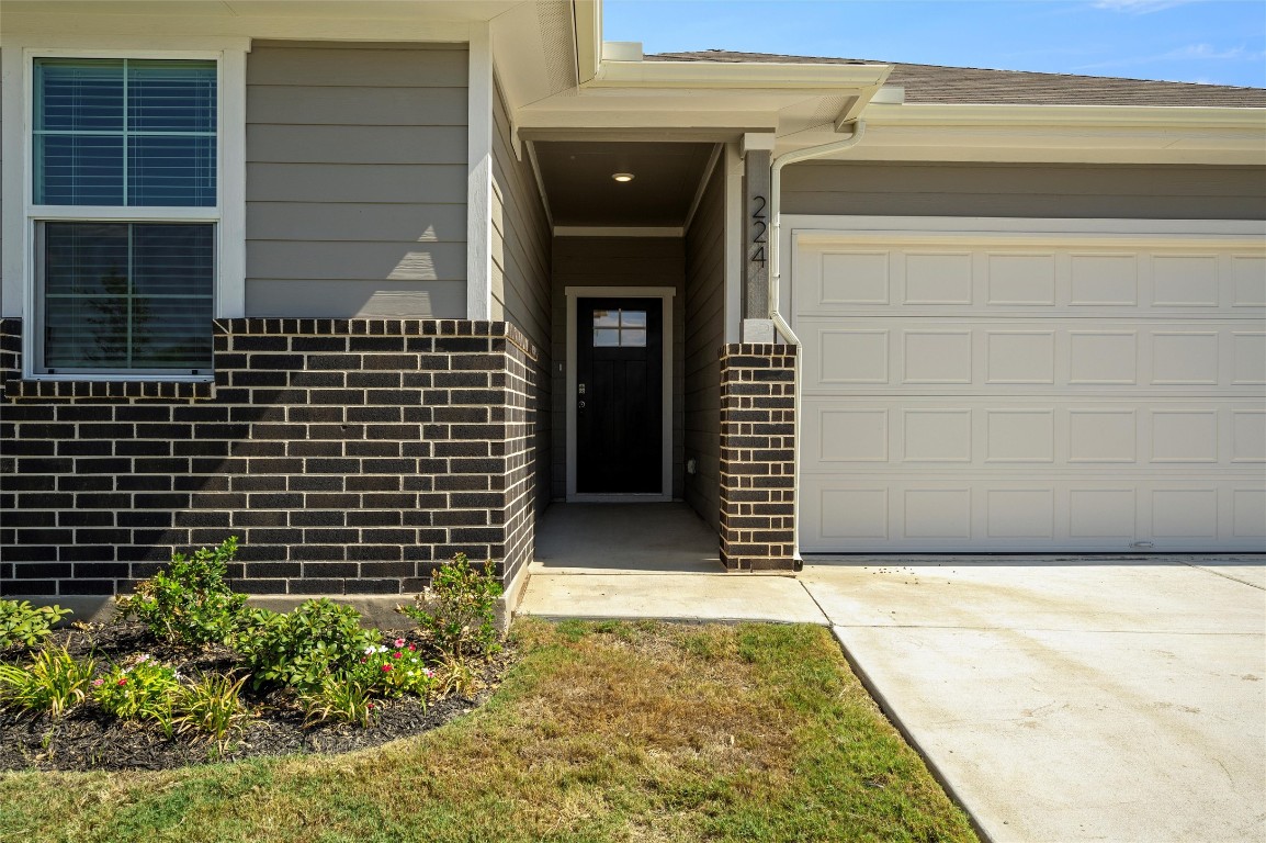 224 Kickapoo Lane Kyle, TX 78640 - Photo 5 of 31 Doorway to property with brick siding, a garage, and concrete driveway