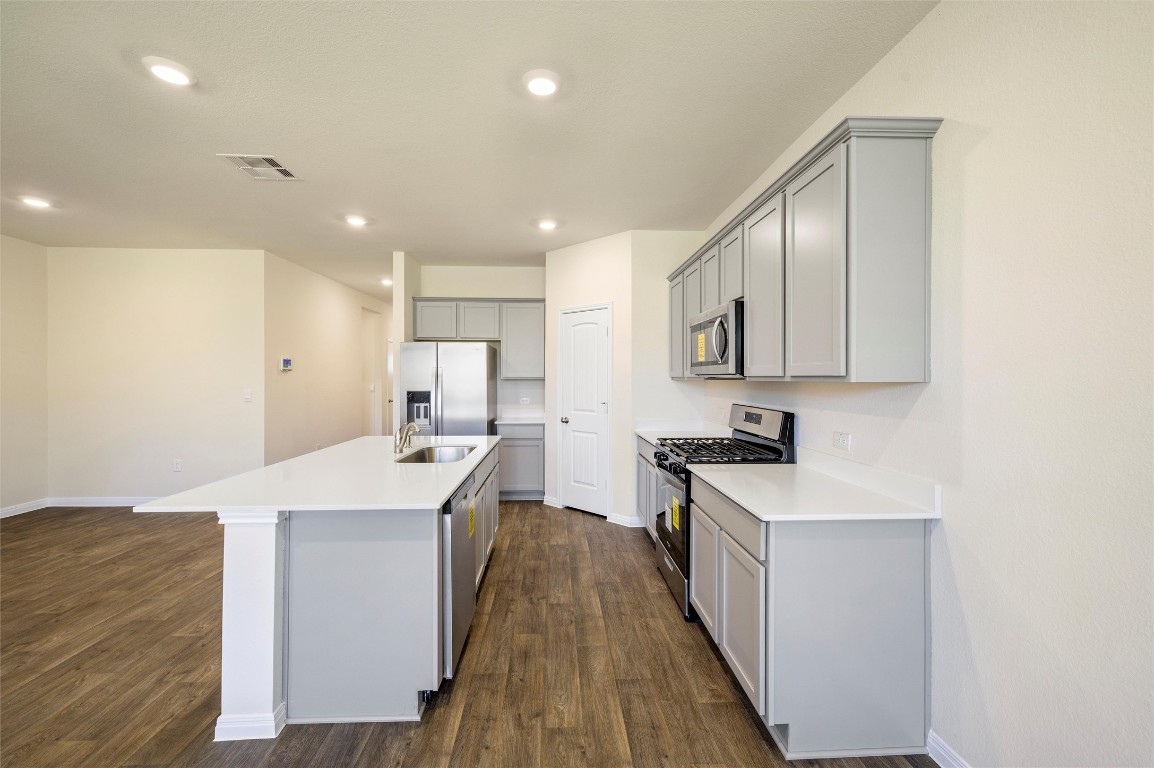 224 Kickapoo Lane Kyle, TX 78640 - Photo 9 of 31 Kitchen with appliances with stainless steel finishes, gray cabinetry, a kitchen island with sink, dark wood-style flooring, and recessed lighting