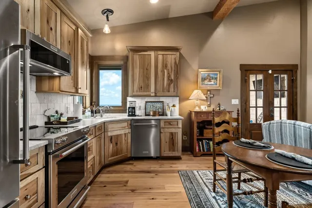 a kitchen with stainless steel appliances granite countertop a stove top oven a sink dishwasher a dining table and chairs with wooden floor