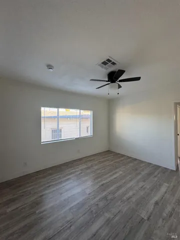 an empty room with wooden floor ceiling fan and windows