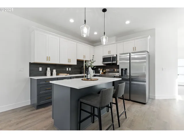 a kitchen with kitchen island granite countertop a refrigerator a stove a sink and white cabinets with wooden floor