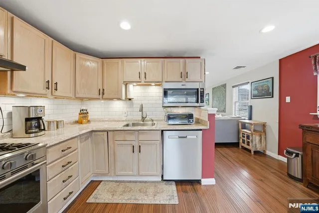a kitchen with stainless steel appliances granite countertop a refrigerator a stove top oven a sink dishwasher and white cabinets with wooden floor