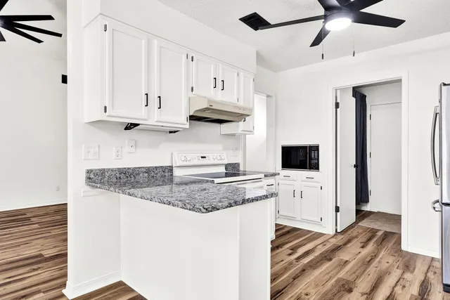 a kitchen with stainless steel appliances granite countertop a refrigerator a sink dishwasher a stove and white countertops with wooden floor