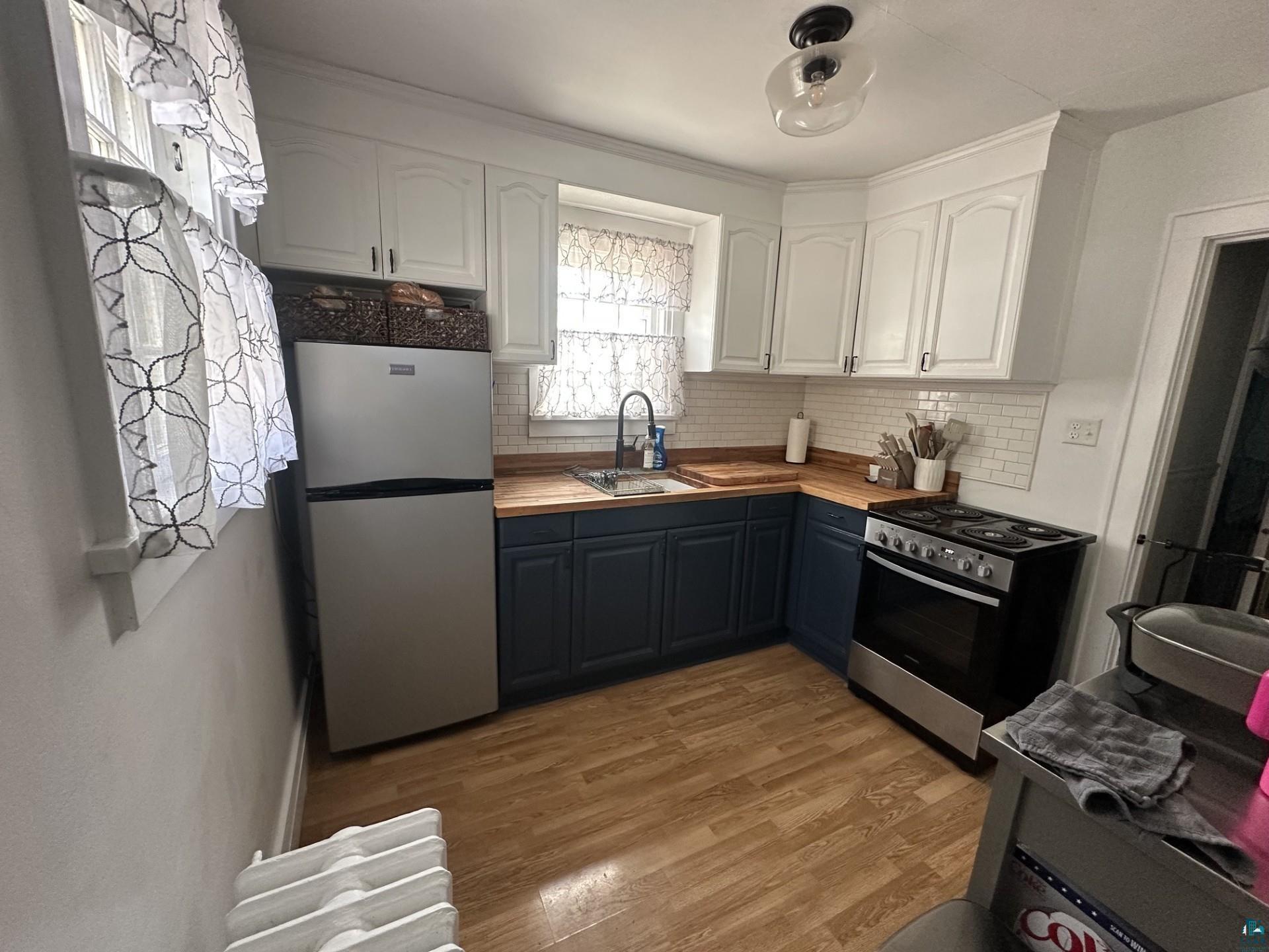 208 Chestnut Street Cloquet, MN 55720 - Photo 13 of 24 Compact kitchen featuring wood-finish flooring, white upper cabinetry, and contrasting blue lower cabinetry