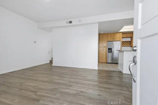a view of empty room with wooden floor and kitchen