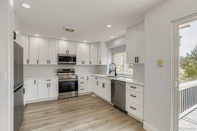 a kitchen with stainless steel appliances granite countertop a stove top oven a sink dishwasher a refrigerator and white cabinets with wooden floor