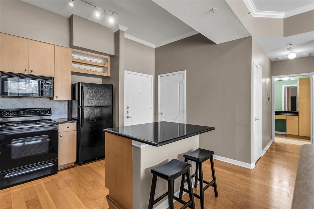 3225 Turtle Creek Boulevard, Unit 10 Dallas, TX 75219 - Photo 10 of 38 Kitchen featuring black appliances, a kitchen breakfast bar, a center island, crown molding, and light brown cabinets