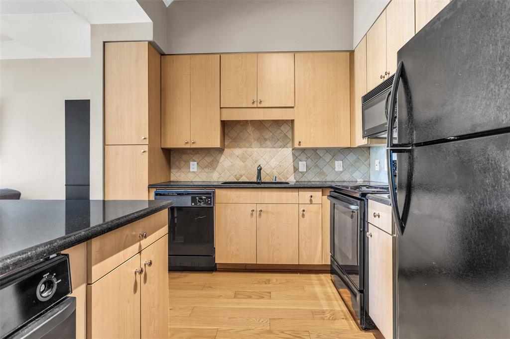 3225 Turtle Creek Boulevard, Unit 10 Dallas, TX 75219 - Photo 14 of 38 Kitchen featuring black appliances, light brown cabinetry, dark stone counters, and light wood-style floors
