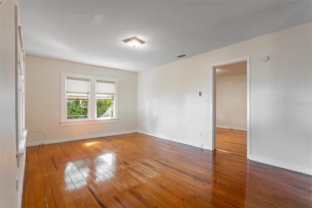 a view of an empty room with wooden floor and a window