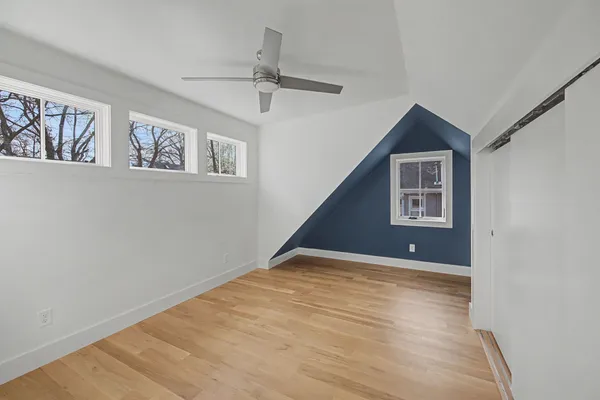 a view of an empty room with wooden floor and a ceiling fan